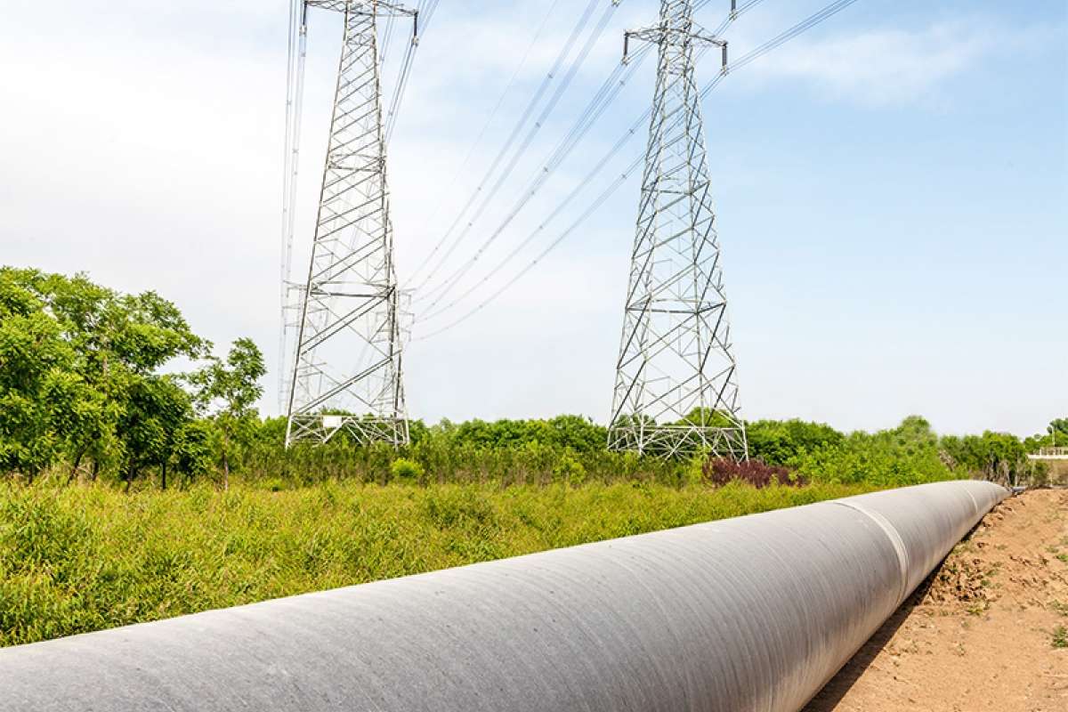Hochspannungsleitung und Pipeline auf grüner Wiese vor Wald.