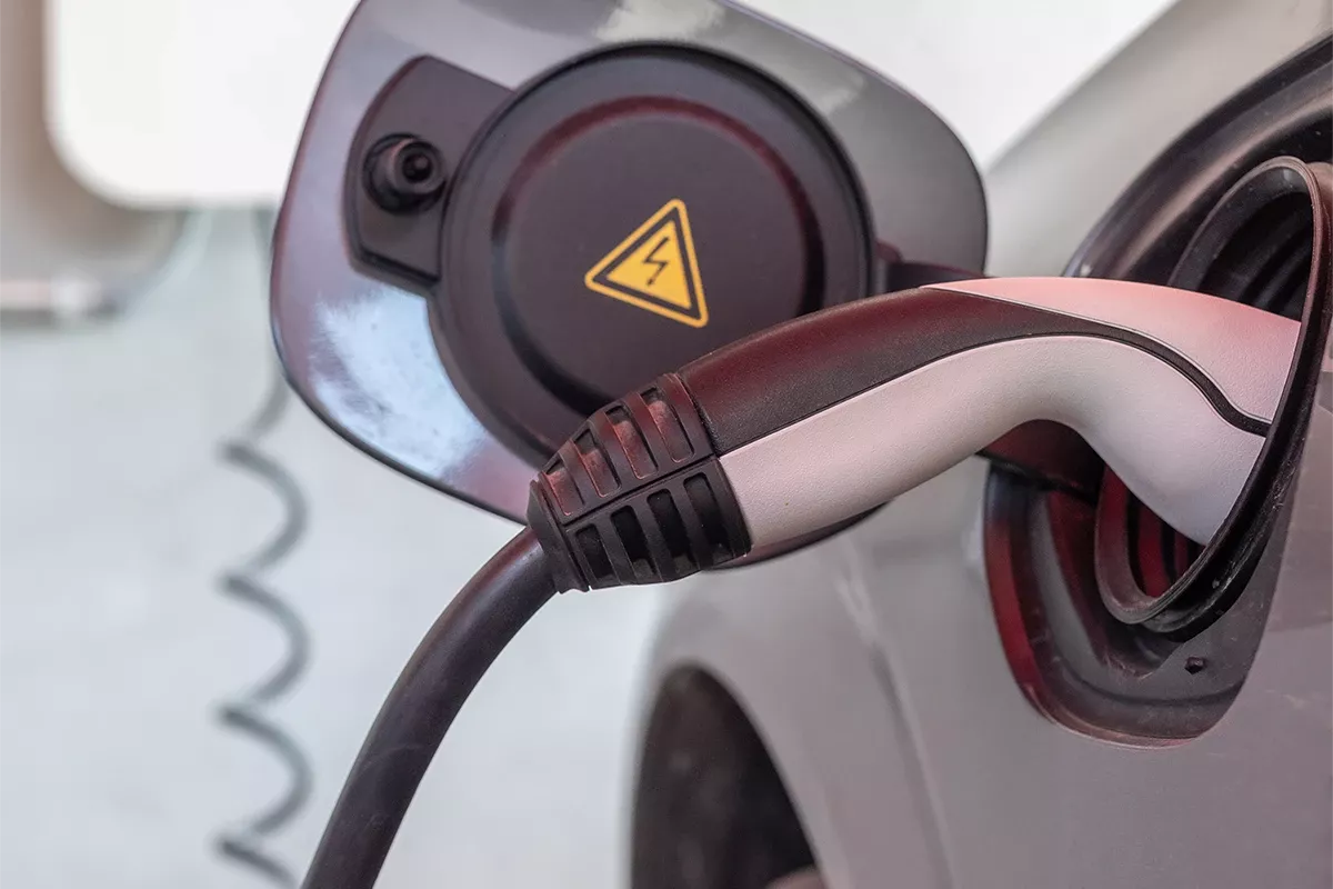 Close-up of an electric car charging connector plugged into the vehicle’s charging port, with a high-voltage warning symbol visible.